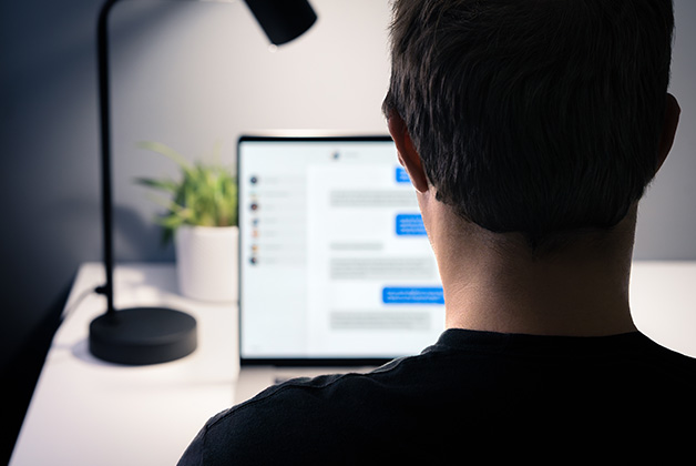 Mężczyzna pokazany od tyłu, siedzący przed biurkiem na którym stoi laptop